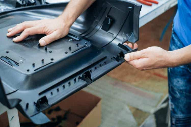 A person works with their hands assembling an intricate black plastic component in an industrial setting