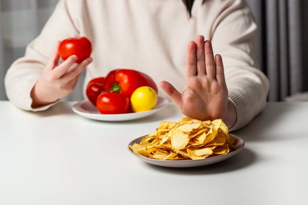 Closeup of woman making stop sign to refuse fried chips for dieting and healthy eating. Vegetable plate. Weight loss concept.