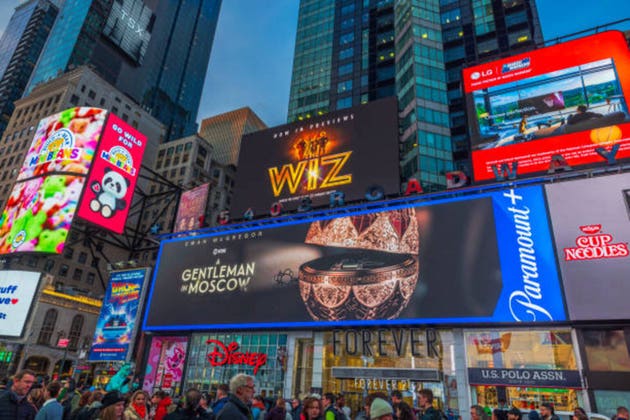 Times Square in New York City with illuminated billboards, digital advertisements and bustling crowd in evening.