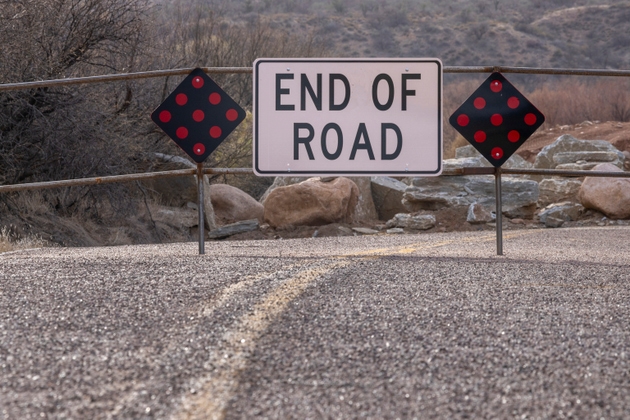 End of road sign on highway below desert mountains