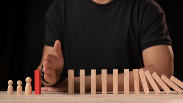 Hand stopping dominos falling in a business crisis decision making and risk management strategies for leadership and strategic planning