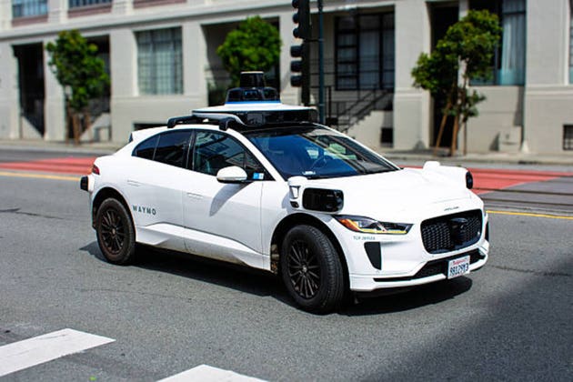 Waymo Jaguar I-PACE equipped with self-driving technology navigates a city intersection, visible sensors and cameras