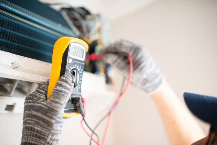 Technician with multimeter repairing air conditioner at home