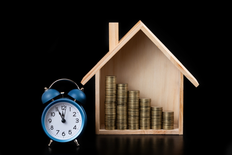 Symbolic wooden house, gold coins and alarm clock on black background