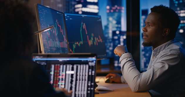 Investment Manager working in office in front of computer with stock market charts visible on displays