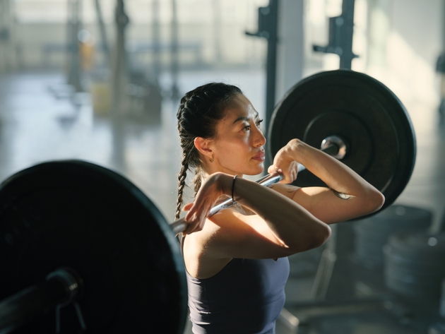 Woman lifting barbell with heavy weights in cross training gym