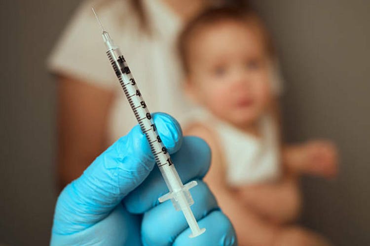 A parent holds a syringe ready for vaccination, focusing on the inoculation process. A child sits nearby, demonstrating a common healthcare practice and the importance of immunization