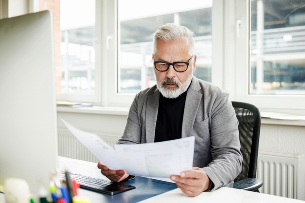 Concentrated senior male professional reviewing financial documents at desk