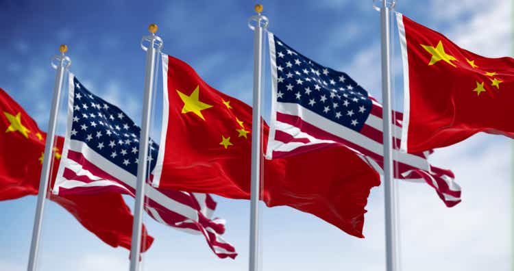 Chinese and American flags waving together against blue sky. 3D render