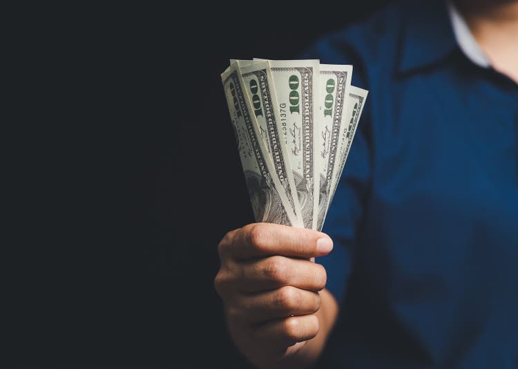 Close-up of a hand offering cash in a bundle of US dollars.