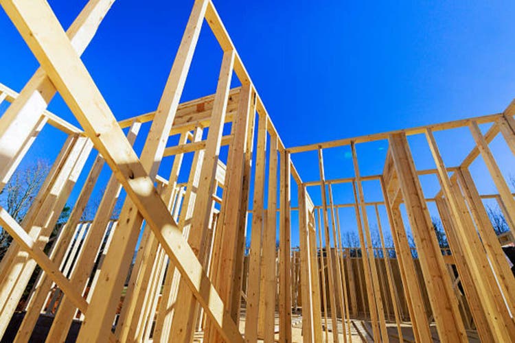 Construction site features wooden framework under a clear blue sky in a residential area