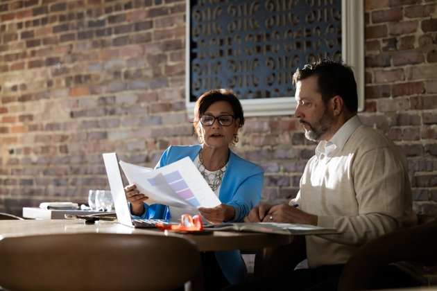 A man and a woman sit and look at papers at a wooden table