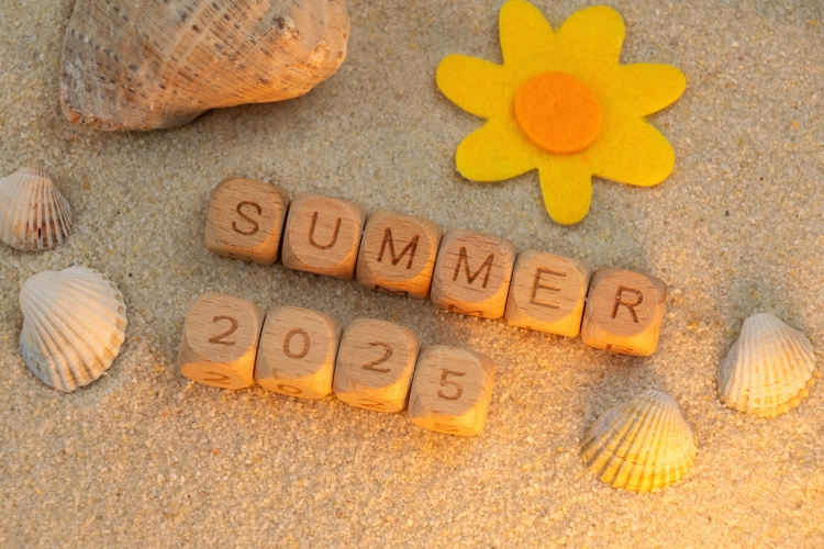 seashells and felt flower on sand background. Wooden blocks spelling Summer 2025.