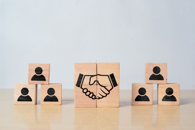 Wooden block with handshake and human icons. Business agreement, partnership, cooperation, and teamwork concept.