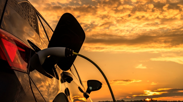 Electric Car Charging Against Vibrant Sunset Sky with Reflective Metallic Finish