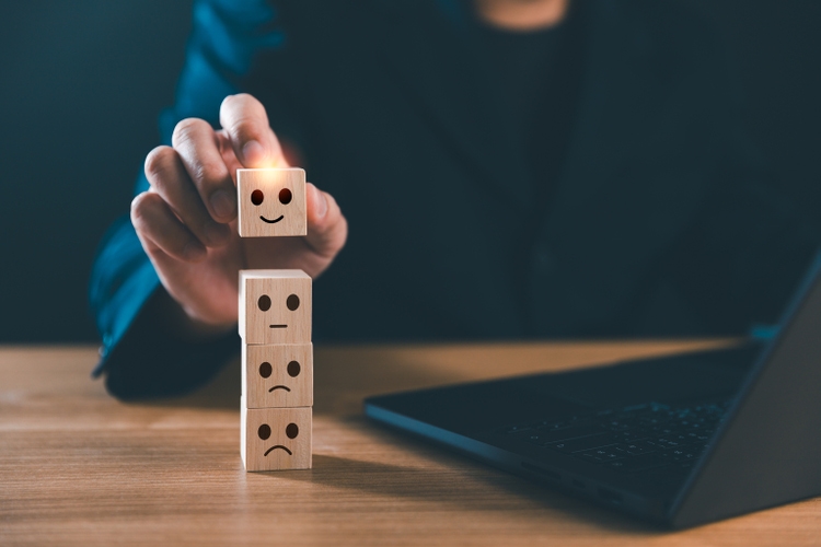 Businessman hand picks a glowing happy face wooden block cube from a stack of emotion icons. The concept of positive customer feedback, customer service satisfaction and excellent user experience