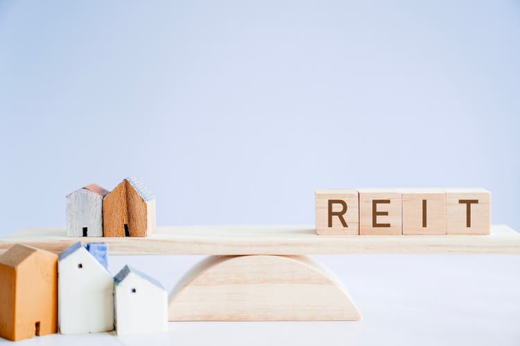 Wooden blocks with REIT and houses on balance scale, Real Estate Investment Trust comparison, hedge money during inflation concept