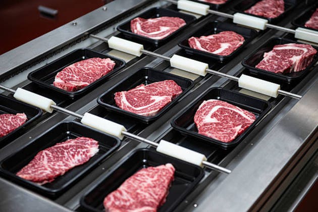 Steaks on a conveyor belt being packaged in a food processing plant