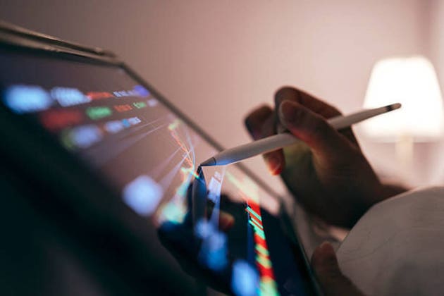 Close-up of a woman using a tablet in bed tracking the technical movement of a stock chart on a computer screen.