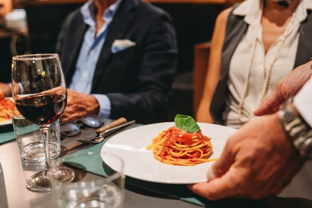 Garçom servindo espaguete com molho de tomate e manjericão para clientes elegantes em um restaurante