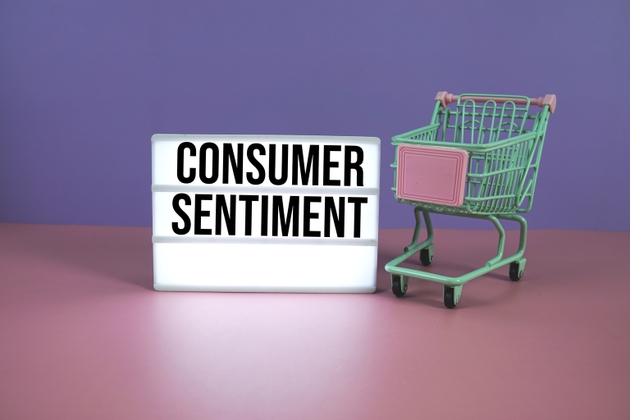 Consumer Sentiment text on LED lightbox with trolley shopping cart on pink and purple geometric background