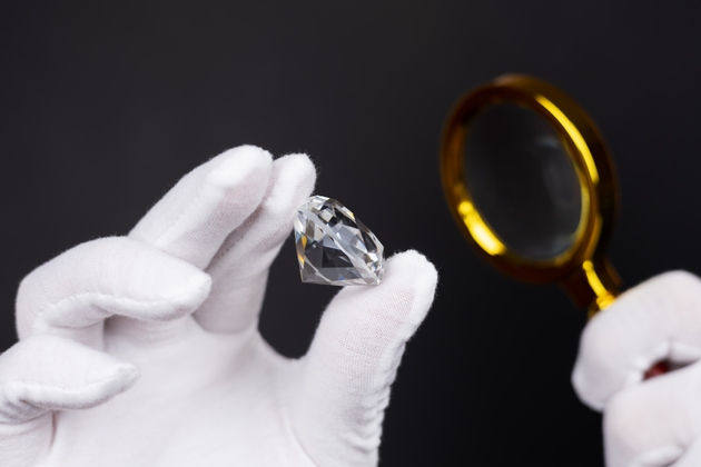 Man jeweller examines polished diamond through magnifier. Buyer checking diamond.