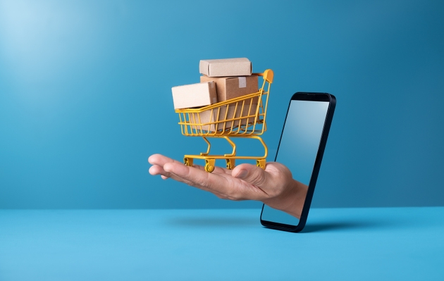 Mini shopping cart with cardboard boxes on hand through smartphone on blue background. Delivery service,online shopping concept.