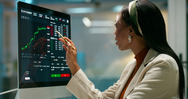 Woman, computer screen and trading charts at office, point and review for growth with profit at agency. African person, investor and monitor for stats, portfolio and graphs with fintech at company