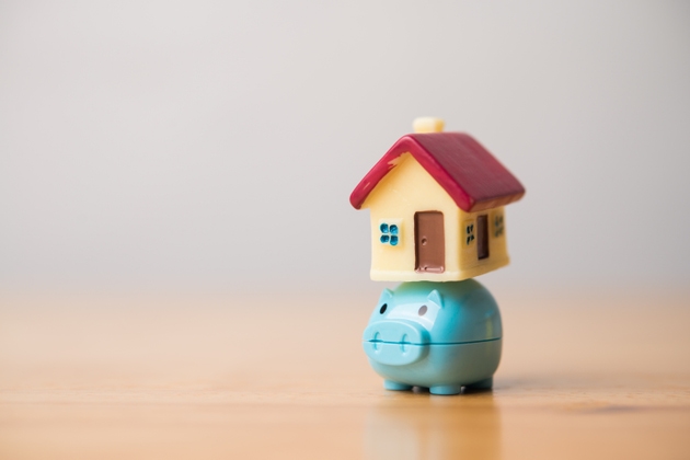 Small house on happy piggy bank on wooden table with white wall background copy space.
