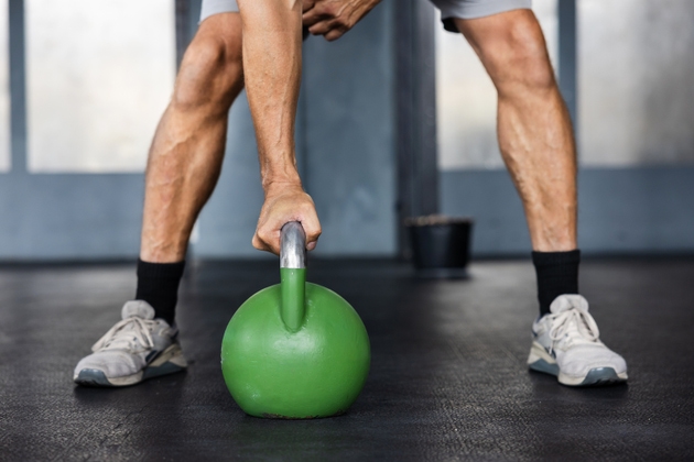 Close up of male athlete gripping heavy green kettlebell during strength training exercise in cross training gym