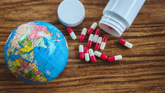 Miniature Globe and Red and White Pills Spilled from a Bottle on Wood, Symbolizing Global Healthcare Crisis, Drug Distribution, and World Health Issues.