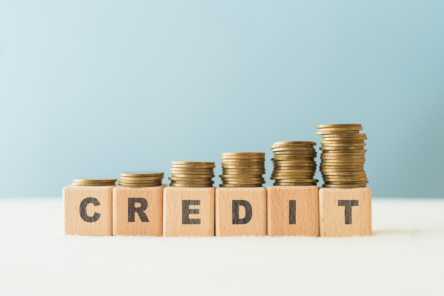 CREDIT text on wooden cube blocks with stack of coins above, blue background, copy space