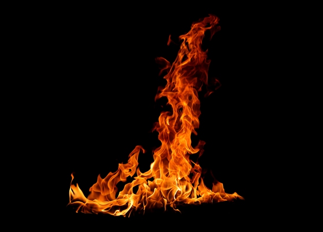Bright orange flame burning on a dark black background, showing detailed fire texture and glowing heat energy. Perfect abstract fire element for backgrounds, design, danger, or energy concept visuals.