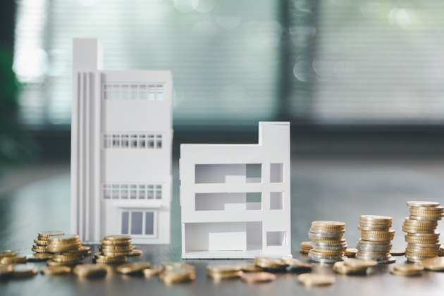 Model house, stacks of coins, calculator, financial documents on a wooden desk represent real estate investment and mortgage planning, highlighting financial growth and strategic planning strategies.