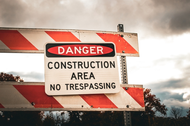 Closeup of a DANGER CONSTRUCTION AREA NO TRESPASSING sign mounted on a striped barrier.