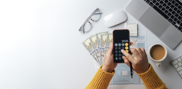 Tax calculation and financial planning concept. Top view accountant using calculator on smartphone with dollar bills, tax forms, laptop and coffee cup for annual tax preparation. Copy space