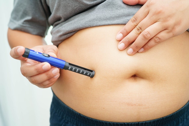 Asian woman injecting herself diabetes injecting insulin in stomach at home.