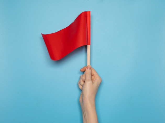 Hand holding a small red flag against a blue background