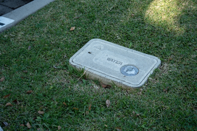 Outdoor water meter box cover with the word WATER embossed on it, set in green grass