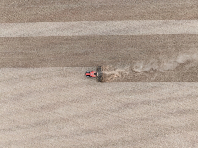 Drone photo directly above a red coloured tractor plowing a dry field in a rural area of Wolverhampton, The Midlands, England, United Kingdom