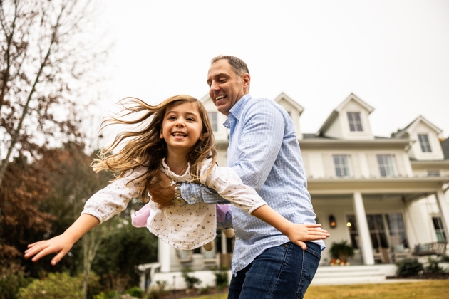 Father giving young daughter an airplane ride in front of suburban home