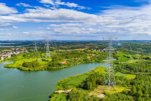 High-voltage transmission towers under blue sky and white clouds