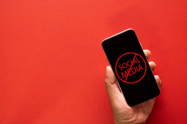 Hand Holding Phone with Banned Social Media Sign on Red Background