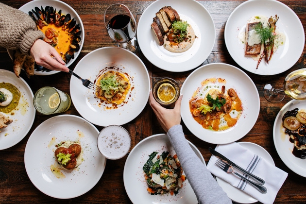 Overhead view of a gourmet dining experience with multiple plates of exquisite food and drinks on a wooden table, capturing a lively dinner party atmosphere.