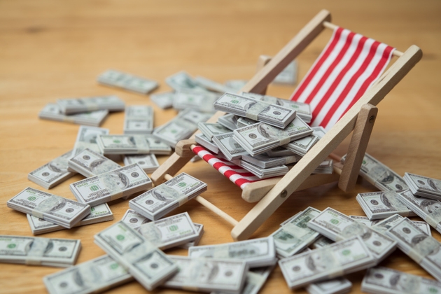 Many US dollar bill banknotes on beach chair and wooden table background.