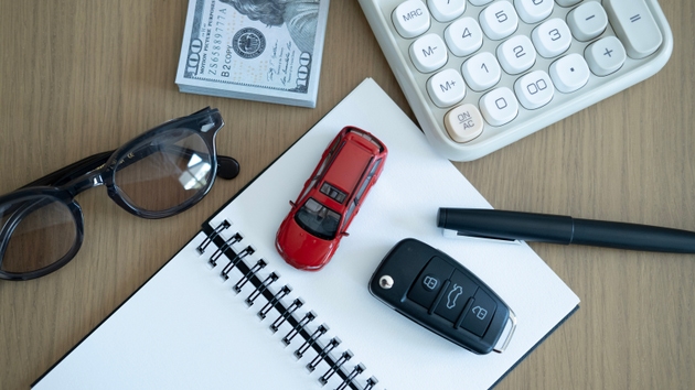 Top view of red toy car on notebook with calculator and money, representing vehicle purchase planning, auto insurance, car loan and financial decision concept.
