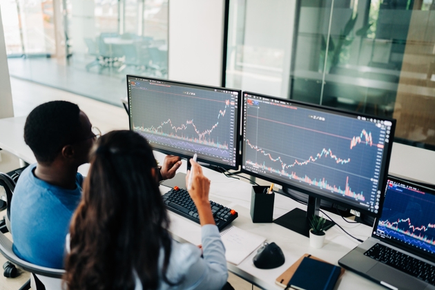 Diverse financial analysts reviewing stock charts on multiple monitors with trading view chart