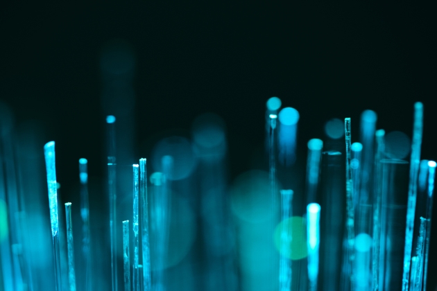 Macro shot glowing fiber optic cable ends emitting soft teal and cyan light against dark background. Concept of high speed internet and data transmission.