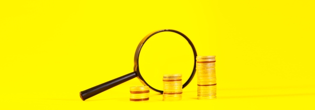 Magnifying glass and golden coins on a yellow background. business concept.