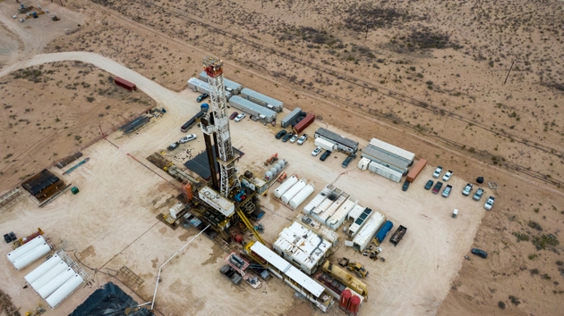 Onshore oil extraction facility with drilling derrick and support infrastructure on high desert landscape. Aerial view of production equipment and storage tanks.